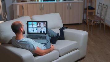 Caucasian male talking about business communication project during call meeting use laptop computer. Focused man lying on sofa in pijamas using modern technology wireless late at night photo