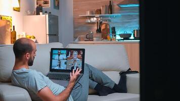 Tired man relaxing on sofa in pajamas during online vidoecall meeting using laptop computer. Caucasian male working at social media project from home because of coronavirus quarantine late at night photo