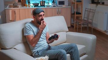 Frustrated man with sleep mask losing videogame competition using wireless controller. Disappointed pro gamer lying on sofa in front of television late at night in kitchen photo