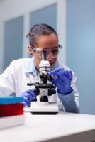 Microbiologist woman looking into medical microscope analyzing virus disease results discovering pharmacology infection. Researcher pharmacist examining bacteriology test experiment in laboratory photo
