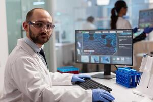 Portrait of scientist man looking at camera sitting in modern equipped laboratory. Scientist doctor examining virus evolution using high tech typing on computer chemistry tools for scientific research. photo
