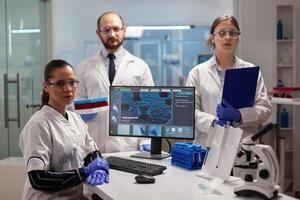 Team of scientists sitting in laboratory looking at camera in modern equipped lab. Group of doctors examining virus evolution using high tech for scientific research, vaccine development. photo