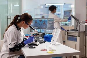 Biotechnology scientist looking through microscope analyzing genetical material. Medicine, biotechnology researcher in advanced pharma lab, examining virus evolution. photo