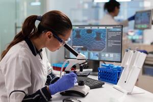 Healthcare scientist researcher vaccine looking at sample through microscope to check for mutations. Medicine, biotechnology researcher in advanced pharma lab, examining virus evolution. photo