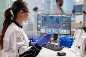 Chemistry doctor analysing blood sample and typing on computer while coworker opening door using digital computer. Healthcare scientist working in modern laboratory using modern technology. photo