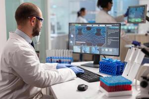 Man scientist working to develop a new vaccine in modern equipped laboratory, typing at computer. Group of biochemistry doctors examining virus evolution using high tech for researching treatment. photo