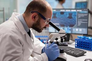 Male scientist looking under microscope at virus sample in medical development laboratory. Specialists working on medicine, biotechnology research in advanced pharma lab. photo