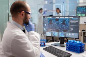 Thoughtfull doctor analyzing virus evolution on computer screen wearing protection glasses. Scientists examining vaccine evolution in medical lab using high tech, chemistry tools for scientific research. photo
