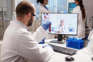 Reseacher holding blood sample discussing treatment with doctor during virtual call. Scientist examining vaccine evolution using high tech researching treatment, health innovation, staff colaboration. photo