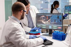Group of scientists working in modern equipped laboratory pointing on computer desktop. y pointing on computer desktop. Chemists stuff analysing virus evolution using high tech technology for treatment research. photo