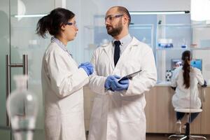 Scientists coworkers using digital tablet working in medical research laboratory, analysing biochemicals samples, talking. Scientific lab for medicine, microbiology development with advanced equipment. photo