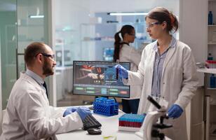 Medical chemists disscussing about vaccine development holding test tube with blood sample. Scientist working with DNA scan image in modern equipped laboratory using high tech technology. photo