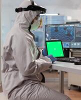 Chemist man wearing protection suit holding tablet with green mockup. Team of microbiologists doing vaccine research writing on device with chroma key, isolated display. photo