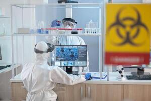 Team of scientist working to develope treatment for virus in lab dresed in ppe suit. Group of doctors examining vaccine evolution using high tech for diagnosis against covid19. photo