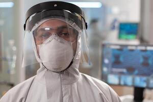 Tired laboratory doctor in protection suit and looking at camera. Team of scientits examining virus evolution using high tech and chemistry tools for scientific research, vaccine development. photo