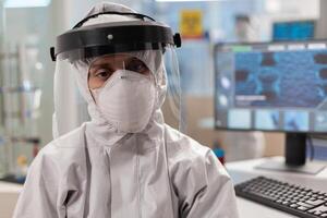Portrait of tired scientist in coverall looking at camera sitting in modern equipped laboratory. Team of scientits examining virus evolution using high tech and chemistry tools for scientific research, vaccine development. photo