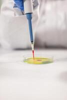Close up of scientist dropping blood sample using micropipette dressed in ppe suit. Chemist in coverall working with various bacteria, tissue for antibiotics research. photo