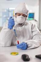 Scientist dressed in ppe suit taking blood sample using micropipette. Scientist dressed in ppe suit taking blood sample Chemist in coverall working with various bacteria, tissue blood samples for antibiotics research. photo