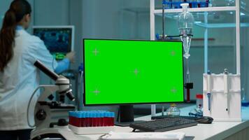 Desktop computer with green screen, mock up on display placed on desk in scientific laboratory while woman medical research scientist analysing virus evolution at digital monitor conducting experiment photo