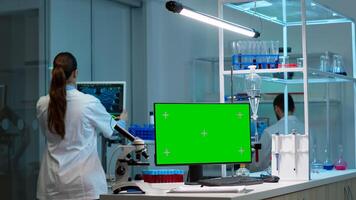 Team of scientists working in background of modern laboratory using computer with green screen, mockup display, chroma key monitor, analysing experiment evolution, high tech development lab. photo
