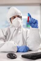 Close up of blood sample while medical researcher looking at it dressed in ppe suit. Scientist examining vaccine evolution using high tech technology for treatment development against covid19 virus. photo
