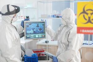 Team of scientist looking at virus evolution standing in lab danger zone dressed in ppe suit. Group of doctors examining vaccine evolution using high tech for diagnosis against covid19. photo
