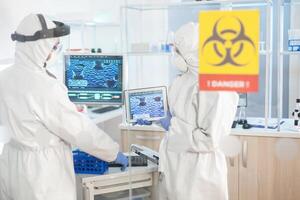 Scientist in laboratory danger zone using tablet pc dressed in ppe suit. Group of doctors examining vaccine evolution using high tech for diagnosis against covid19. photo