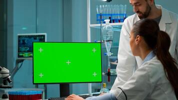 Medical research scientists using desktop computer with green screen mock up template in applied science laboratory. Lab engineers in white coats conduct experiments working with chroma key display photo