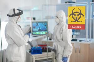 Danger zone sign in medical laboratory and scientist working dressed in ppe suit. Group of doctors examining vaccine evolution using high tech for diagnosis against covid19. photo
