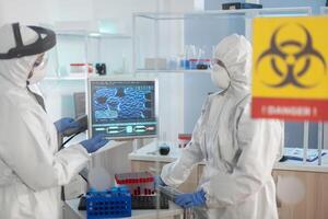 Scientists in ppe suit talking behind the glass wall working in danger area of lab. Group of doctors examining vaccine evolution using high tech for diagnosis against covid19. photo