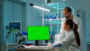 Female research scientist has conversation with man bioengineer next to a desktop computer with green screen mock up. They look at chroma key pc template in a modern science laboratory. photo