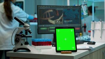 Scientist standing at monitor in background analysing virus evolution while tablet with mock-up green screen working in front. Man lab researcher examining vaccine developent bringing blood samples photo