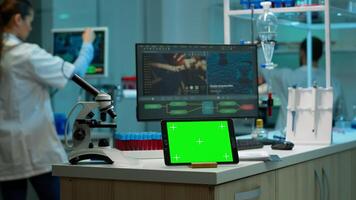 Notepad with green screen working in labooratory with mock up monitor, chroma key display while professional engineer testing virus evolution in background. High tech development lab. photo
