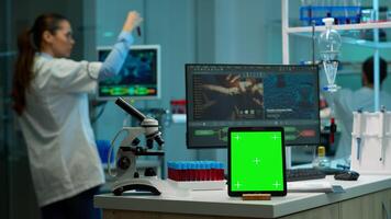 Team of scientists working in background of modern laboratory using tablet with green screen, mockup display, isolated chroma key monitor, analysing experiment evolution, high tech development lab. photo