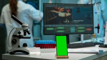 Display phone with green screen, mock up on template placed on desk in scientific lab while team of medical researcher scientists analysing virus evolution at digital monitor conducting experiment photo