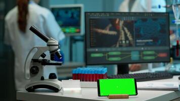 Microbiologist bringing blood samples in modern lab putting them near smartphone working with green chroma key screen placed on desk. Team of biotechnology scientists developing drugs in background photo
