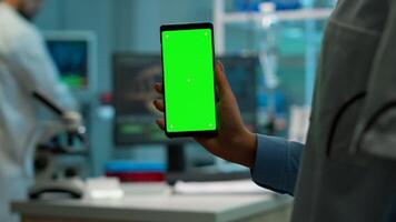 Chroma key isolated display on smartphone used by scientist woman in lab cabinet and colleagues in white coat bringing blood sample. Scientist using mobile phone with mockup green screen photo