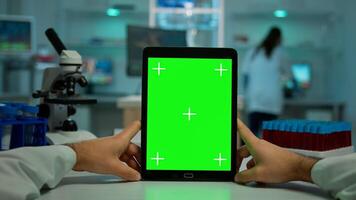 POV shot of chemist using tablet with green screen in biological laboratory. Medical worker wearing white coat in clinic working with notebook with chroma key on isolated display in medical lab photo