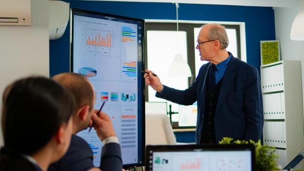 Experienced project leader analysing financial presentation during business conference in brainstorming room using digital devices. Multiethnical team working in professional startup company during meeting photo