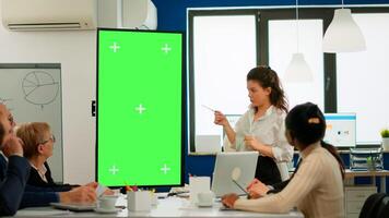 Young leader briefing diverse businessteam standing in front of meeting table analysing financial statistics, looking at greenscreen display. Multiethnic workers planning project on chroma key desktop photo
