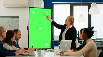 Diverse business team sitting at meeting table analysing financial statistics, looking at green screen display while senior leader explaning. Multiethnic workers planning project on chroma key desktop photo