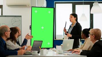Leader of company presenting financial plan using mockup display in front of diverse team brainstorming. Manager explainig project strategy on green screen monitor with chroma key desktop in boardroom photo