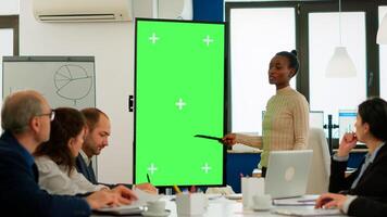 Diverse woman standing in start up office discussing strategy with green screen monitor in front of business partners. Manager explaining to multiethnic team project chroma key display mock up desktop photo