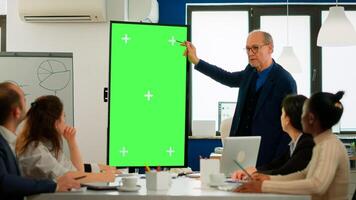 Mature businessman analysing annual financial reports standing in conference room pointing at green screen monitor. Leader explainig project strategy using mockup pc chroma key display in boardroom photo