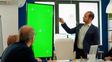 Young man leader of company presenting financial strategy using green screen mockup display in front of diverse team brainstorming. Manager explainig project showing monitor with chroma key desktop photo