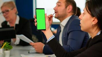 Businesspeople analysing annual financial reports sitting at desk while employee holding phone with green screen monitor. Leader explainig project strategy using greenscreen pc with chroma key display photo