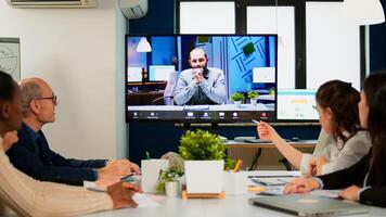 Manager man talking with colleague using call for virtual meeting, employees sitting in broadroom looking tv screen. Diverse team planning strategy during conference, online brainstorming photo