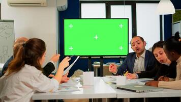In corporate office meeting room stands green mock-up screen TV or interactive digital whiteboard in horizontal mode. Multiethnical businesspeople working, brainstorming in professional start up photo