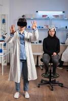 Neuroscience doctor gesturing wearing vr goggles during brain science research, patient with neurology scanner in laboratory. Doctor searching diagnosis, experiment , eeg , medicine lab. photo