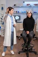 Scientist doing brain analysis using headset with sensors on patient explayning diagnosis. Monitor shows modern brain study. Wearing neuroscience headset analysis. photo